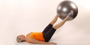 Memegang bola gimnastik di antara kaki yang diangkat mengembangkan penekan bawah